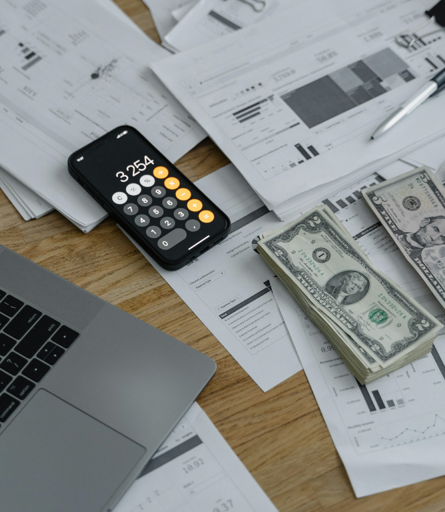 Person performing payroll with calculator, laptop, and money.