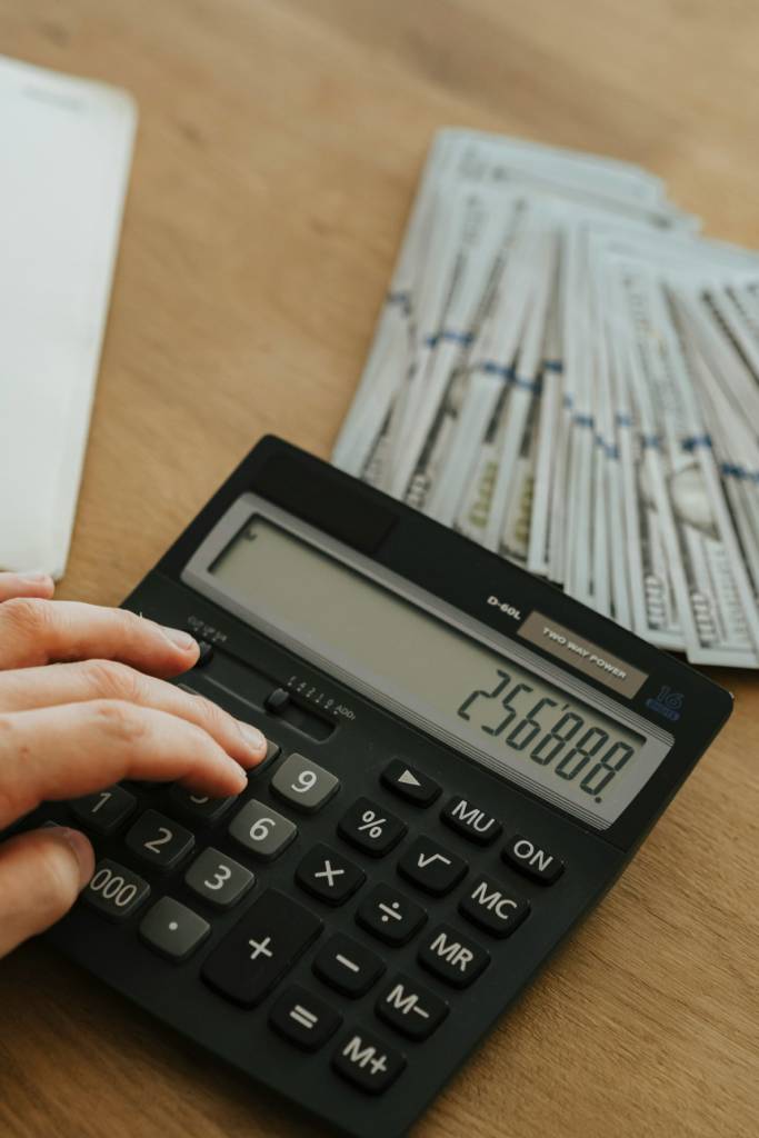 Person typing on a calculator next to a stack of money.